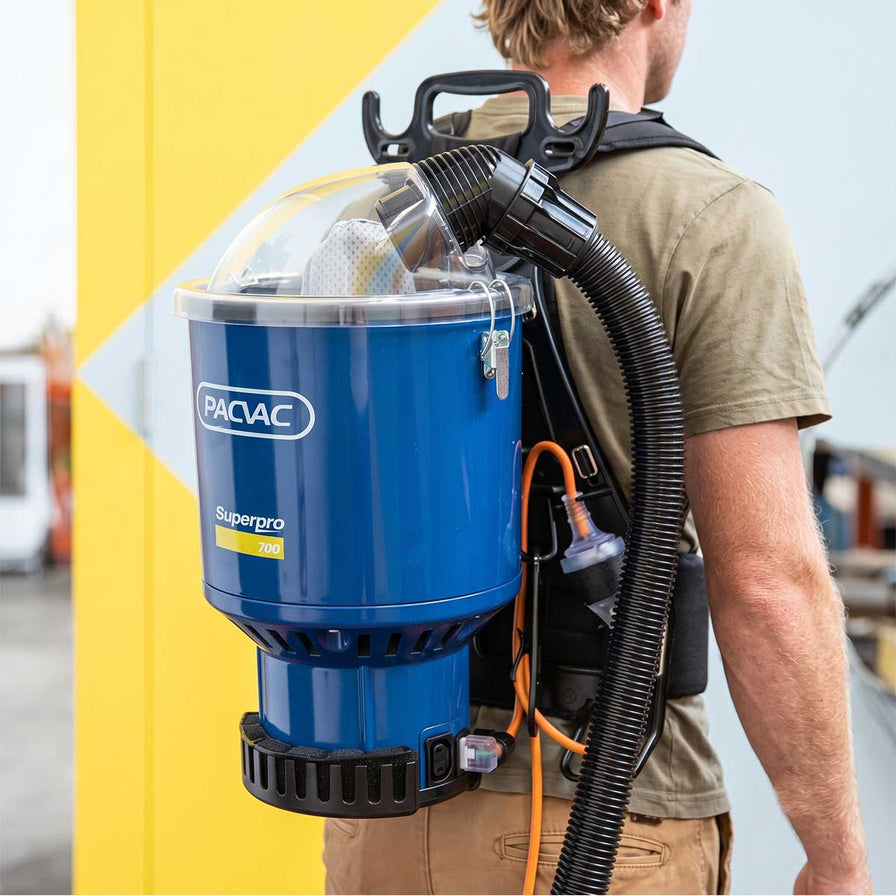A man wearing a blue and blue Pacvac Superpro 700 backpack vacuum cleaner.